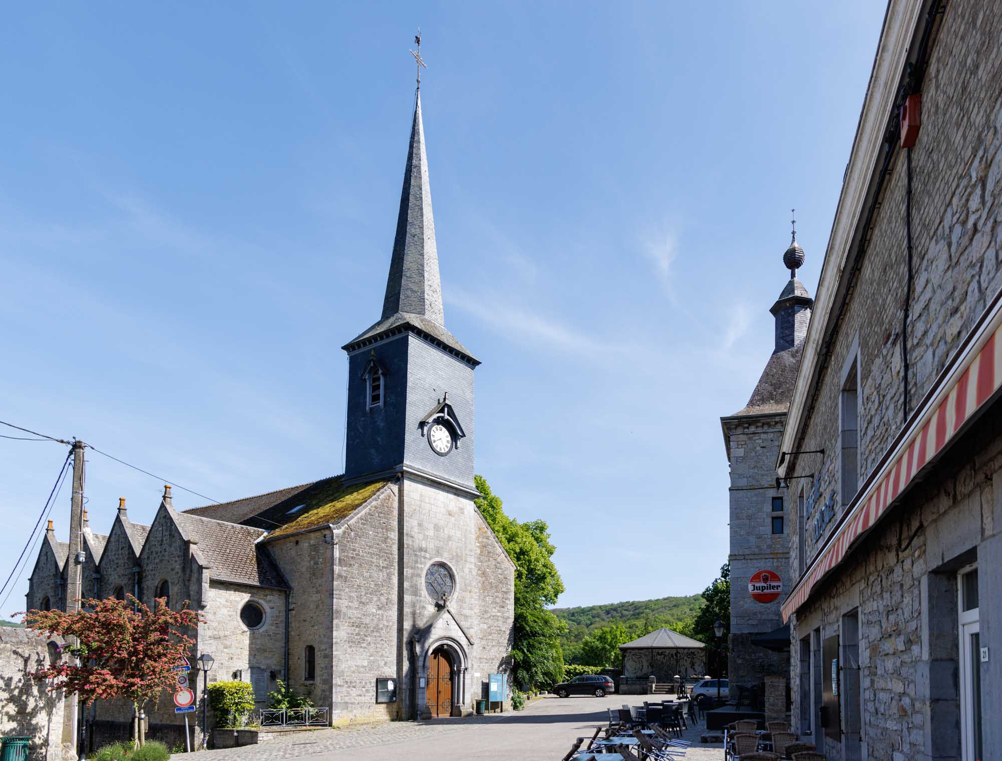 Église de Viroinval sur la place du village, avec maisons en pierre et ciel dégagé.
