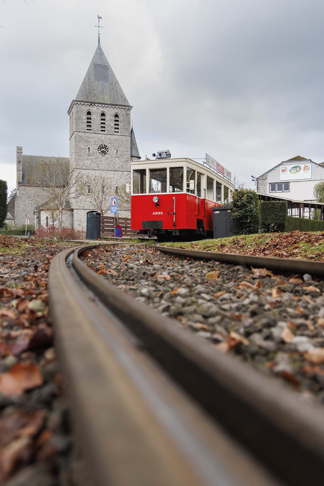 Rode toeristische tram in Han-sur-Lesse voor de dorpskerk, bij bewolkt weer
